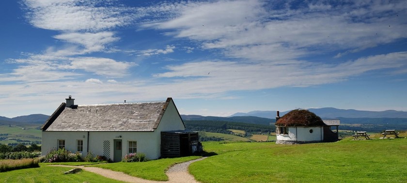 Moniack Mhor writing retreat. A single-storey croft in the Scottish Highlands. It's a sunny day and there's a blue sky with just a few white clouds