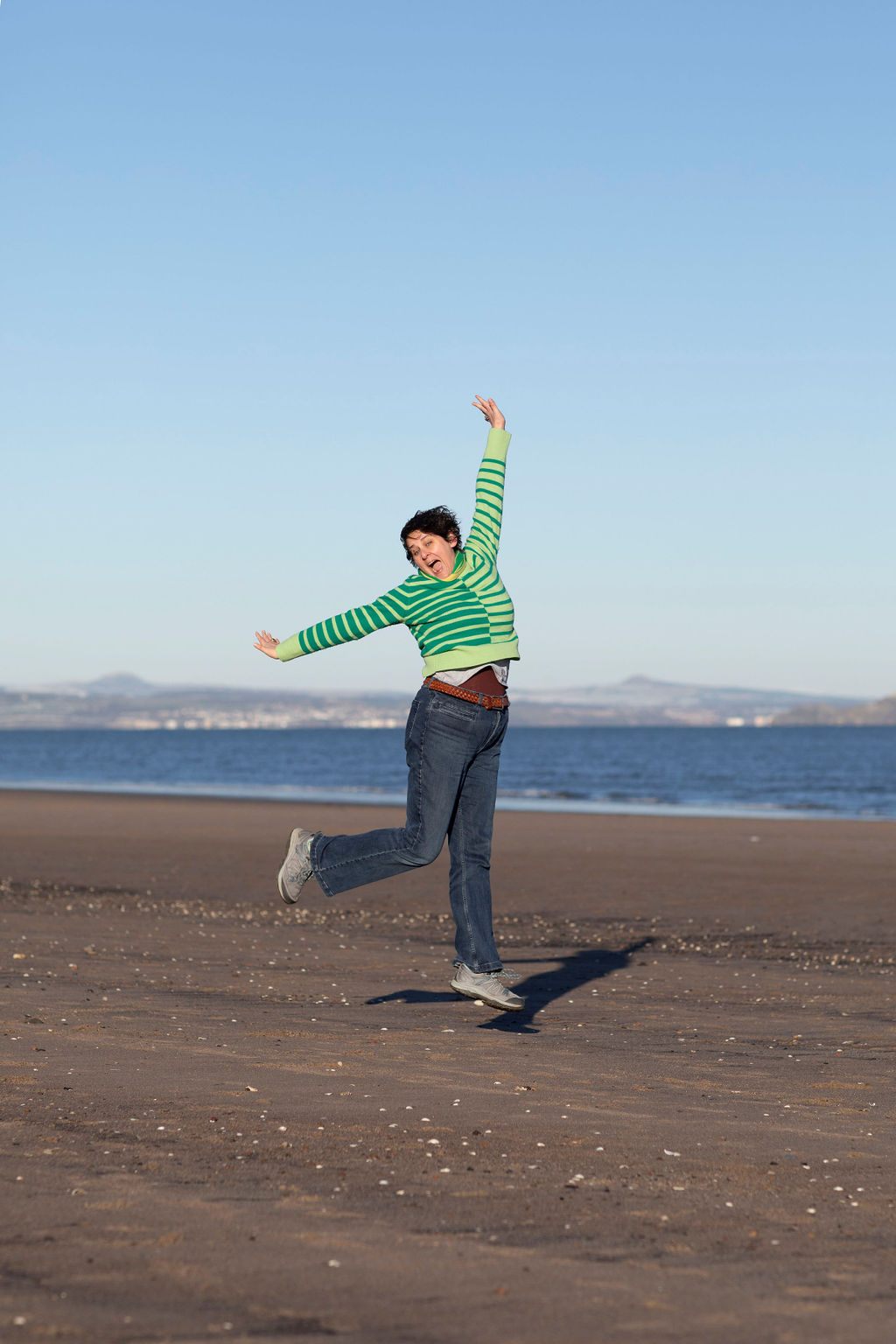 woman in green jumper and jeans jumping on beach