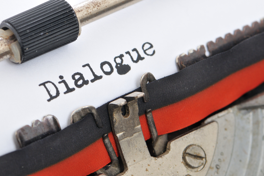 An old fashioned typewriter with a black and red ribbon and the word 'Dialogue' typed on a piece of white paper