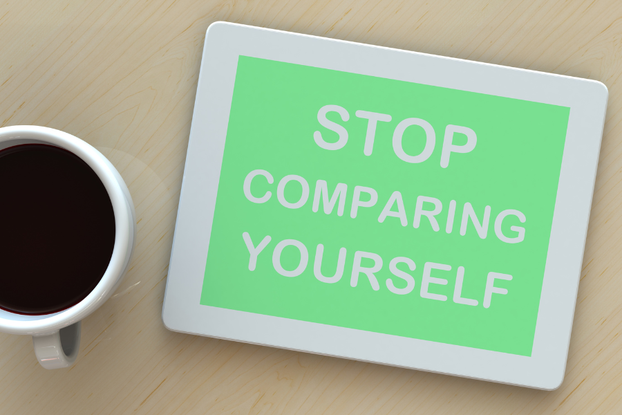 A cup of coffee next to a sign with a light green background with the words 'stop comparing yourself' written in white letters