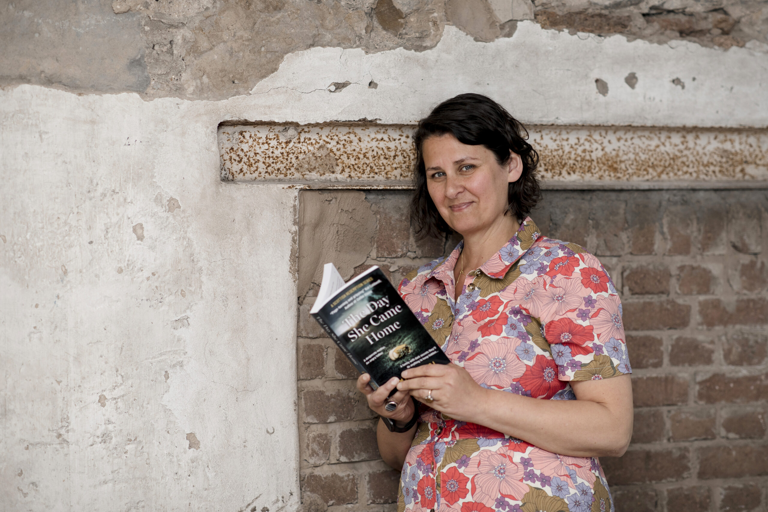 Emma Dhesi leaning against a wall and reading a book