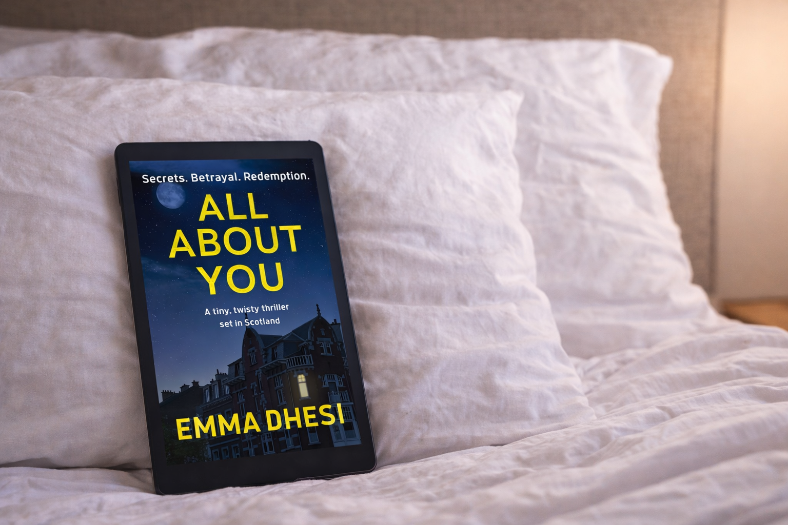 E-reader displaying All About You by Emma Dhesi resting on a bed beside white pillows